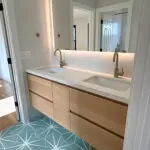 Double sink vanity with teal/aqua geometric floor tiles.