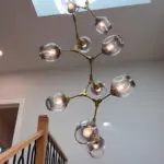 Brass chandelier over oak staircase under skylight.
