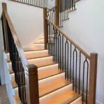 Modern oak floating staircase with LED risers and arched black iron balusters.